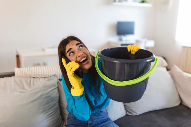 woman using pail to collect water leaking from roof ceiling